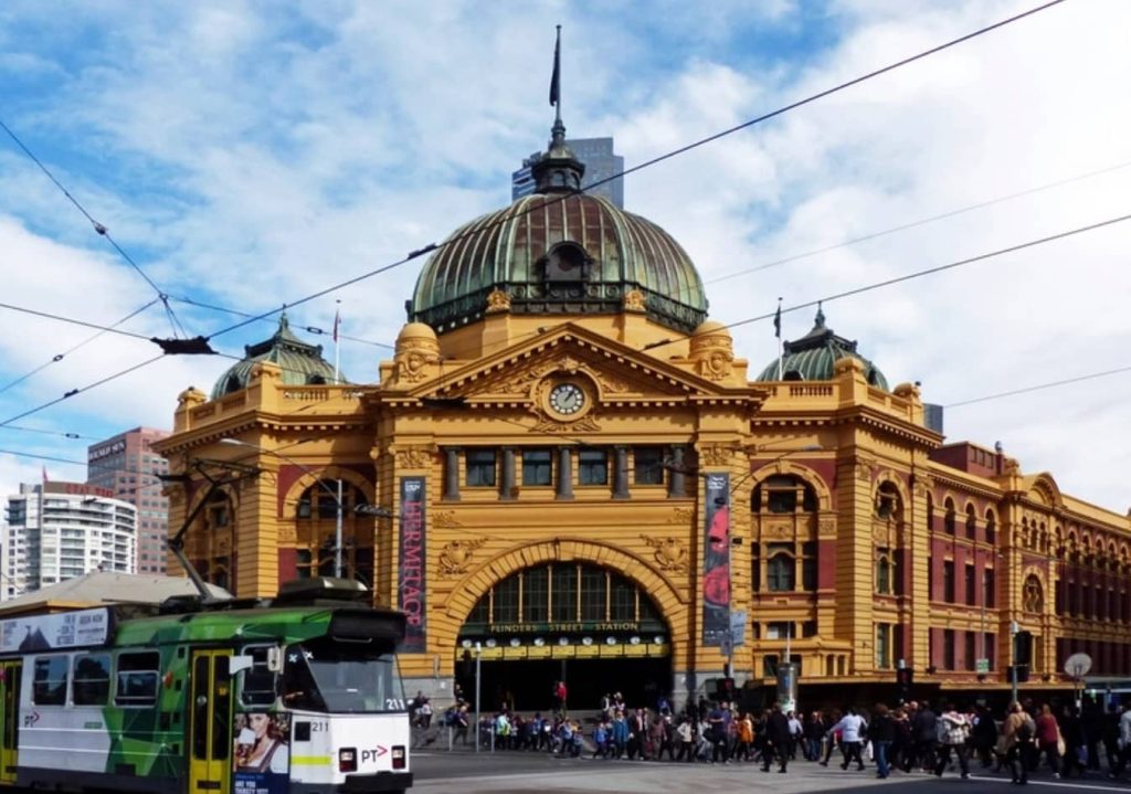 A historic yellow Flinders Street Station building with a tram in the foreground representing a central Melbourne campus transport hub.