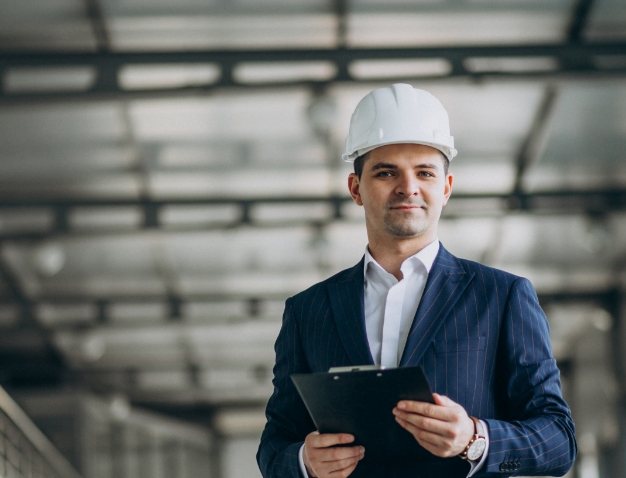 A professional male project manager wearing a hard hat and holding a clipboard, representing leadership in construction or technical management.