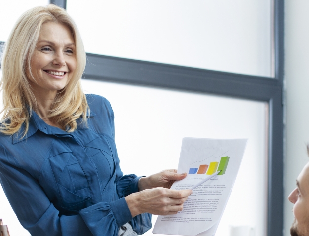 A smiling professional woman discussing business data charts with a colleague in a modern office environment.