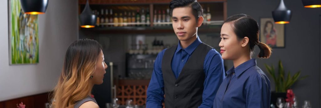 Two hospitality trainees in corporate uniform uniforms listening to a presentation about restaurant service and guest relations.